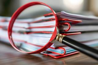 Foto: Lupe vor Dokumentenstapel